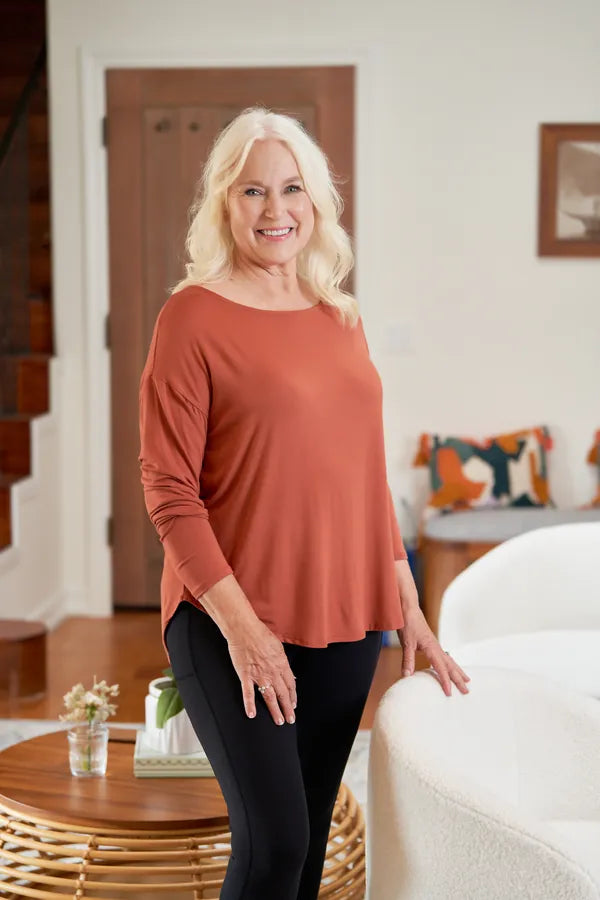 Woman with silver hair in a rust bamboo dolman long sleeve tee in a sunlit living room