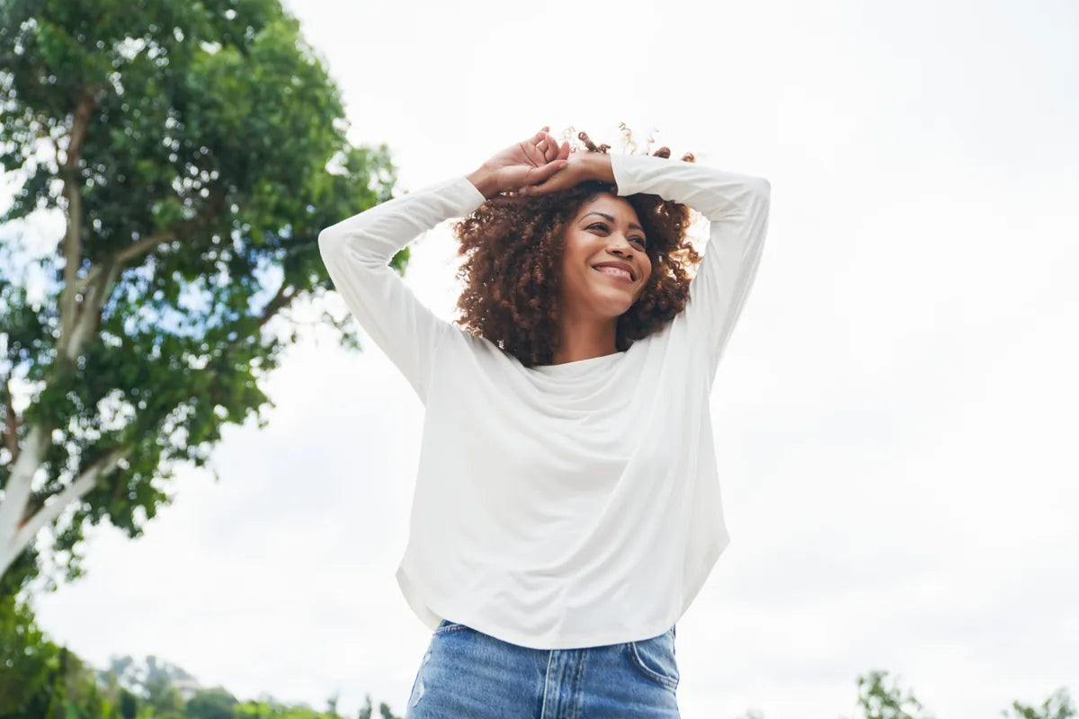 Woman laughing with her arms above her head in a soft white bamboo long sleeve tee