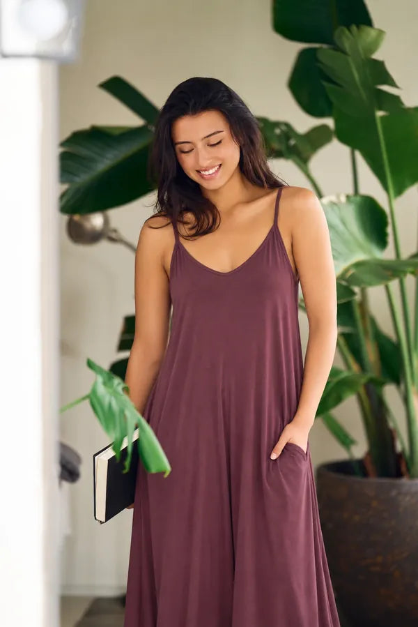 Woman smiling in a plum bamboo slip dress among tall green plants