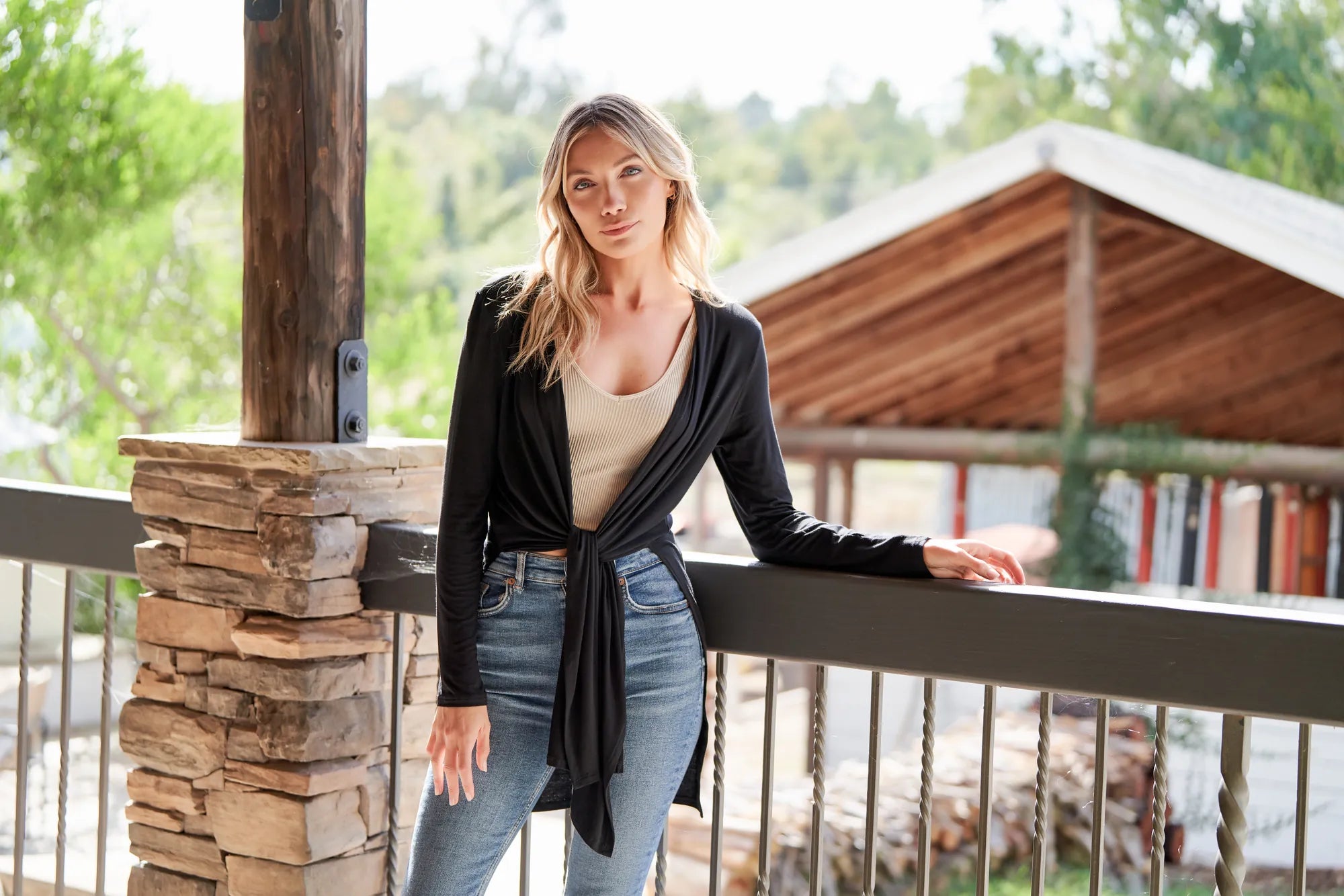 Woman in a black bamboo yoga wrap leaning on a porch rail above a green valley